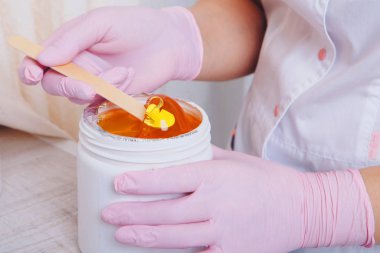 Depilasyon için balmumu yakın plan. Kız kavanozdan kozmetik ürünler çıkarıyor. Kozmetik işlemler için tahta çubukla el. Şekerleme: bacaklarda sıvı şeker ile sonlanma