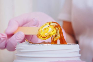 Depilasyon için balmumu yakın plan. Kız kavanozdan kozmetik ürünler çıkarıyor. Kozmetik işlemler için tahta çubukla el. Şekerleme: bacaklarda sıvı şeker ile sonlanma