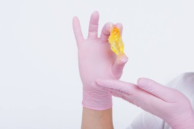 Yakından tüy dökmek için balmumu. Kız kozmetik ürünler sergiliyor. Doktorun eldivenli eli. Şekerleme: Sıvı şekerli saç kesimi. Bu daha az acılı bir tüy dökücü.