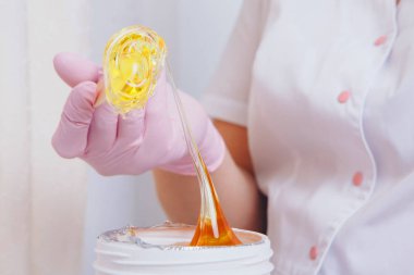 Depilasyon için balmumu yakın plan. Kız kavanozdan kozmetik ürünler çıkarıyor. Kozmetik işlemler için tahta çubukla el. Şekerleme: bacaklarda sıvı şeker ile sonlanma