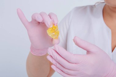 Yakından tüy dökmek için balmumu. Kız kozmetik ürünler sergiliyor. Doktorun eldivenli eli. Şekerleme: Sıvı şekerli saç kesimi. Bu daha az acılı bir tüy dökücü.