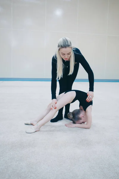 A woman teaches a girl to sit on the twine. the trainer teaches some stretching exercises. the girl is engaged in recreational gymnastics. sports exercises and stretching: athletics