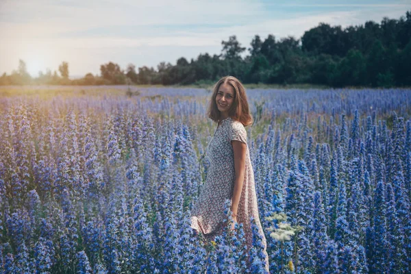 a girl in a loose dress with her hair down walks through a flower meadow. A woman enjoys life among purple flowers . The concept of summer, warmth, freedom, and the scent of spring