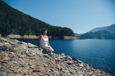 Kız gölün yanındaki kayalıklarda oturuyor. Kumsalda güneşlenen bir kadın. Eğlence ve turizm kavramı.