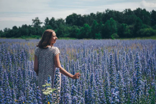 a girl in a loose dress with her hair down walks through a flower meadow. A woman enjoys life among purple flowers . The concept of summer, warmth, freedom, and the scent of spring