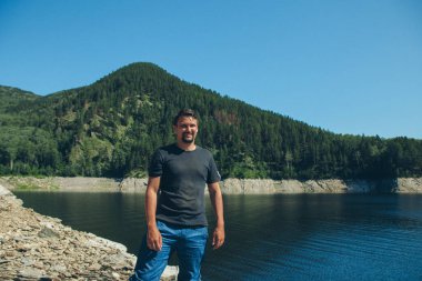 Adam gölün yanındaki kayalıklarda oturuyor. Sahilde güneşlenen bir adam. Eğlence ve turizm kavramı.