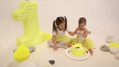 Doğum günü kutlaması: iki küçük kız beyaz arka planda kek yiyor. Çocuk yiyecekle kaplı. Tatlılığı mahvettim. 1 numara, suni çiçekler ve beyaz toplar. Uzayı kopyala Doğum günü konsepti, tatiller, yemek pişirme