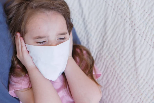 Portrait of a child who covered her face with a mask. A girl is home-schooled. The concept of quarantine, self-isolation, protection from coronavirus, virus, fear of disease, treatment, medicine