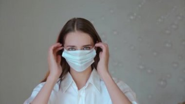 Tıbbi maske takan, beyaz arka planda mutlu bir kadının portresi. Tıbbi ekipmanların tanıtımı. Kız dansı. Karantina, kendini izole etme, koronavirüsten koruma, virüs, hastalık korkusu, tedavi, ilaç