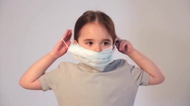 Tıbbi maske takan beyaz arka planda bir çocuğun portresi. Tıbbi ekipmanların tanıtımı. Kız işaret ediyor. Karantina, kendini izole etme, koronavirüsten koruma, virüs, hastalık korkusu, tedavi, ilaç