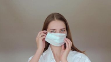 Beyaz arka planda tıbbi maske takan bir kadının portresi. Tıbbi ekipmanların tanıtımı. Kız işaret ediyor. Karantina, kendini izole etme, koronavirüsten koruma, virüs, hastalık korkusu, tedavi, ilaç