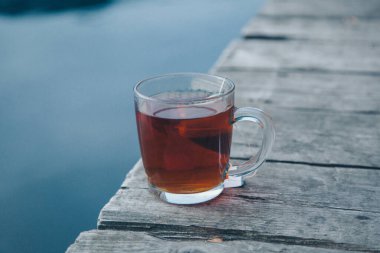 Rıhtımda su kenarında bir fincan siyah çay. Güçlü sıcak içecekler, seyahat, rahatlama kavramı
