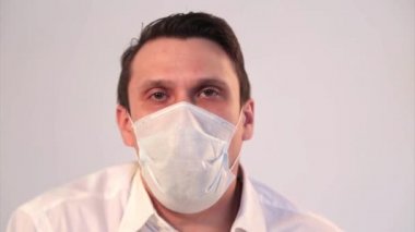 Tıbbi maske takmış beyaz arka planda bir adamın portresi. Tıbbi ekipmanların tanıtımı. Hasta öksürüyor. Karantina, kendini izole etme, koronavirüsten korunma, virüs, hastalık korkusu, tedavi, ilaç, akciğer hasarı