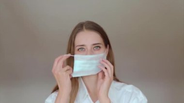 Beyaz arka planda tıbbi maske takan bir kadının portresi. Tıbbi ekipmanların tanıtımı. Kız işaret ediyor. Karantina, kendini izole etme, koronavirüsten koruma, virüs, hastalık korkusu, tedavi, ilaç