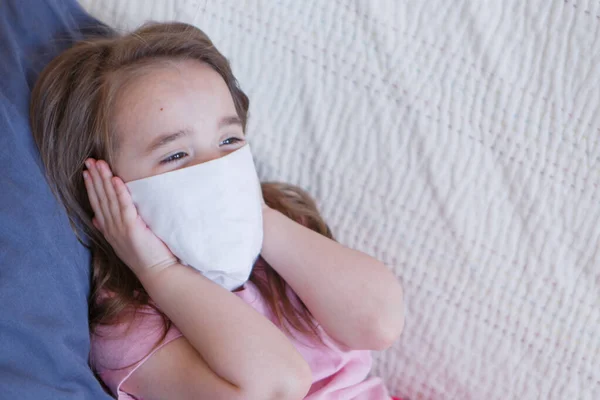 Portrait of a child who covered her face with a mask. A girl is home-schooled. The concept of quarantine, self-isolation, protection from coronavirus, virus, fear of disease, treatment, medicine