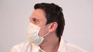 Beyaz arka planda tıbbi maske takan bir adamın portresi. Tıbbi ekipmanların tanıtımı. Adam işaret ediyor. Karantina, kendini izole etme, koronavirüsten koruma, virüs, hastalık korkusu, tedavi, ilaç