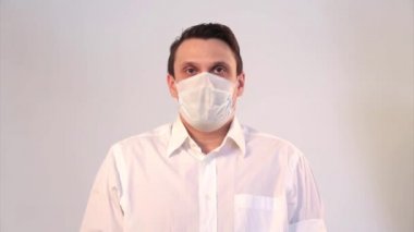 Beyaz arka planda tıbbi maske takan bir adamın portresi. Tıbbi ekipmanların tanıtımı. Adam işaret ediyor. Karantina, kendini izole etme, koronavirüsten koruma, virüs, hastalık korkusu, tedavi, ilaç