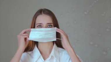 Beyaz arka planda tıbbi maske takan bir kadının portresi. Tıbbi ekipmanların tanıtımı. Kız işaret ediyor. Karantina, kendini izole etme, koronavirüsten koruma, virüs, hastalık korkusu, tedavi, ilaç