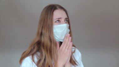 Tıbbi maskeli bir kız elleri önünde katlanmış dua ediyor. Tıbbi ekipmanların tanıtımı. Karantina, kendini izole etme, koronavirüsten korunma, virüs, hastalık korkusu, tedavi, ilaç, din