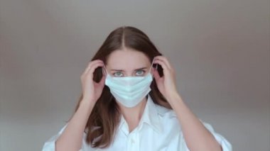 Beyaz arka planda tıbbi maske takan bir kadının portresi. Tıbbi ekipmanların tanıtımı. Adam işaret ediyor. Karantina, kendini izole etme, koronavirüsten koruma, virüs, hastalık korkusu, tedavi, ilaç