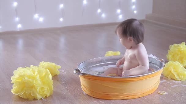 女の子がレモンとグレープフルーツと一緒にお風呂に入っています 黄色の花の間の盆地で子供が洗う 子供時代 イヴフ 柑橘類療法の概念 — ストック動画