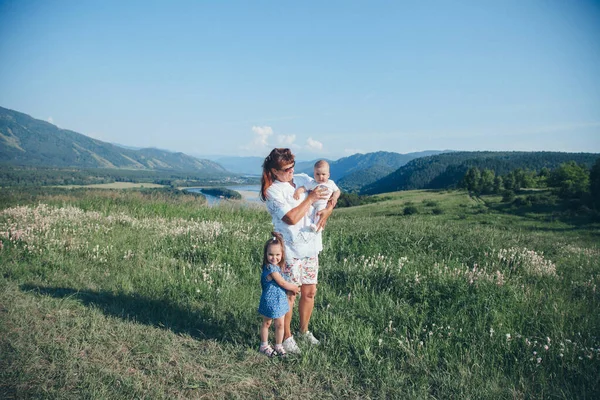 Bebekli bir kadın çayırda yürüyor. Köy evleri, orman ve nehir arka planda. Yaz konsepti, sıcaklık, özgürlük, köy hayatı, güneş yanığı, çocukluk