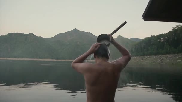 潮湿的人站在湖边 那家伙在用水桶浇水 冷水耗尽了身体 快乐的人经过艰苦的体力劳动后 力量运动的概念 洗澡后的蒸汽 健康的生活方式 — 图库视频影像