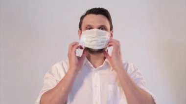 Beyaz arka planda tıbbi maske takan bir adamın portresi. Tıbbi ekipmanların tanıtımı. Adam işaret ediyor. Karantina, kendini izole etme, koronavirüsten koruma, virüs, hastalık korkusu, tedavi, ilaç