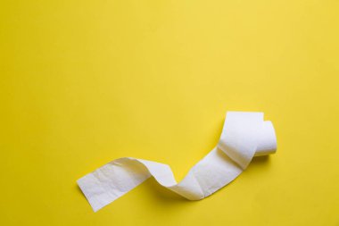 Tuvalet kağıdı sarı arka planda yuvarlanıyor. Kopya uzayındaki günlük nesneler. Coronavirus döneminde hammadde eksikliği. Piyasada popüler bir ürün. Ev için mal teslimatı