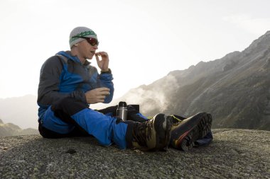 Alpinist duraklar gündoğumu sırasında ve sıcak bir çay hazırlar