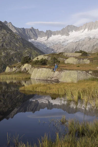 Alpinista faz uma pausa durante um nascer do sol em um lago de montanha nos Alpes suíços — Fotografia de Stock