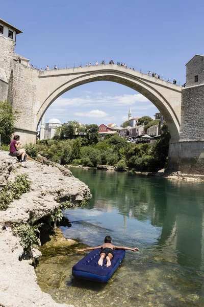 Mostar, Bosna a Hercegovina, 15 července 2017: chlapec leží na nafukovací matrace před historické obloukový most přes řeky Neretvy do Mostaru na krásný letní den — Stock fotografie