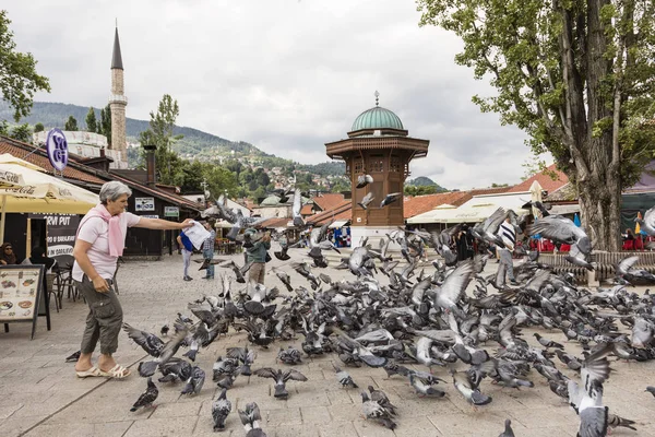 Sarajevo, Bósnia-Herzegovina, 16 de julho de 2017: Mulher alimenta pombos em frente à fonte Sebilj no centro histórico da cidade — Fotografia de Stock