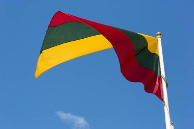 Lithuanian national flag waving on wind against blue cloudy sky clipart