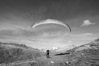 Paraglider pilotu bir kayanın üzerinde durur ve İsviçre Alpleri 'nde Grimsel yakınlarında paraglider' ını dengeler.