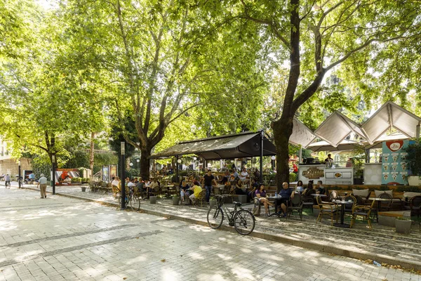 Tiran, Arnavutluk, 8 Temmuz 2019: Tiran 'da ağaçlı bir yaya kenti caddesinde yürüyen insanlar, yan taraftaki bir açık kafedeki insanlar.