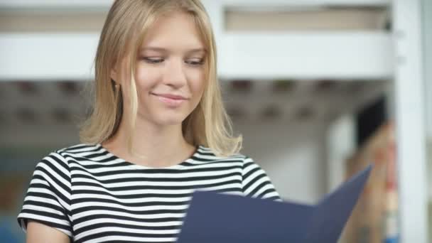 A young girl in a striped sweater holding a blue folder in her hand — Stock Video