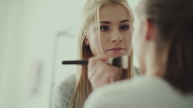 Makyaj sanatçısı bir model ve gülümseyerek boyar. Makyaj için büyük bir fırça kullanır.