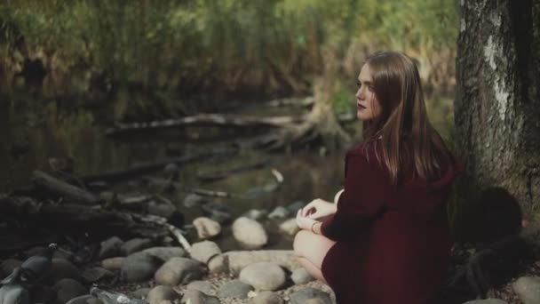 Rapariga senta-se sozinha perto do lago. A menina com cabelos longos alimentando os patos . — Vídeo de Stock