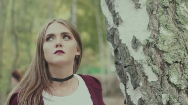 Dziewczynka z duszkami wokół szyi i jasnym makijażu na tle drzew — Wideo stockowe