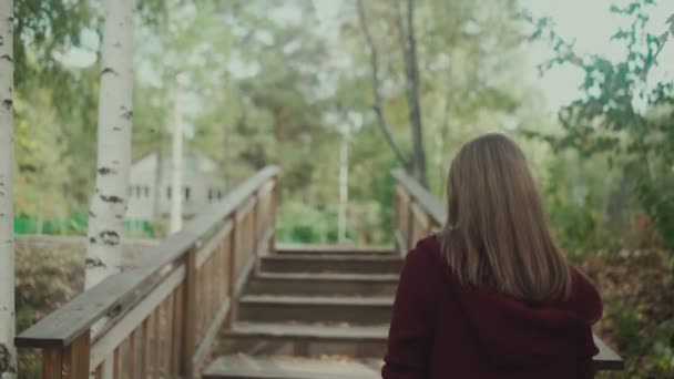 Young girl climbs the stairs in the forest. Maroon cardigan. Walk alone. — Stockvideo