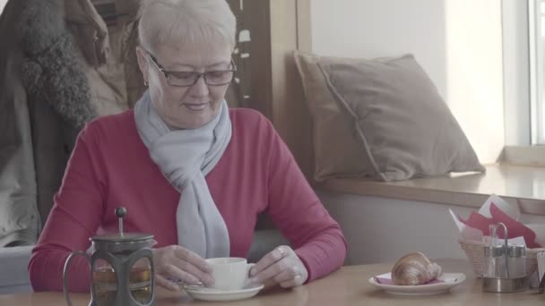 Pensionären ger muggen te till hennes läppar, tar en klunk och ser ut — Stockvideo