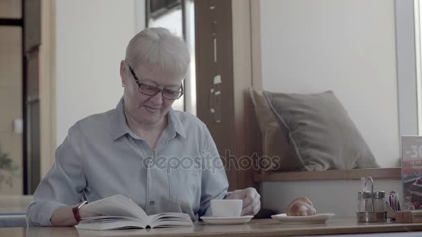 Пенсионер проводит время в кафе, читает интересную книгу — стоковое видео