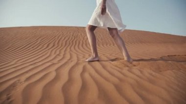 Beyaz elbiseli ince kız çölde kum çıplak ayakla devam ediyor