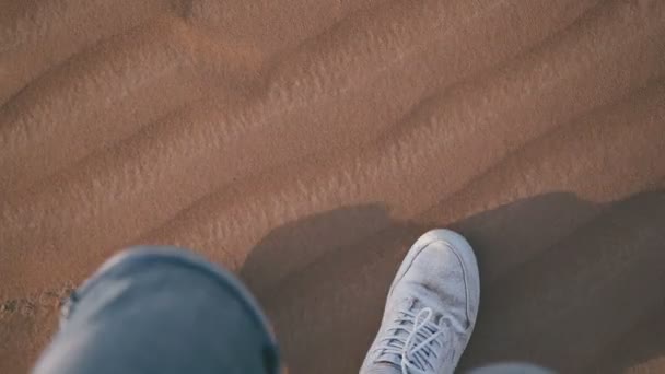 Blick von oben: Der Mann in weißen Turnschuhen geht durch die Wüste — Stockvideo