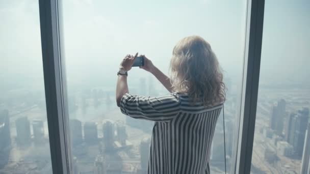 Meisje toeristische staan bij het raam en gefotografeerd op een mobiele telefoon — Stockvideo