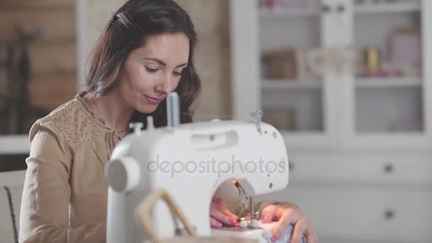 Женщина с темными волосами в бежевом платье занимается шитьем — стоковое видео