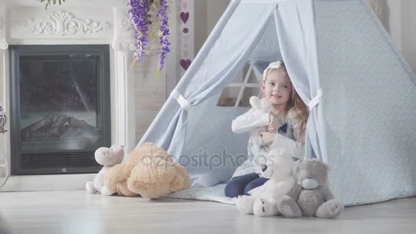 Kleines Mädchen im Tipi-Zelt umarmt ihren Teddybär, Kind und spielt — Stockvideo