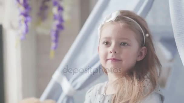 Маленька дівчинка в іграшковому будинку викидає м'яку іграшку і усміхається — стокове відео