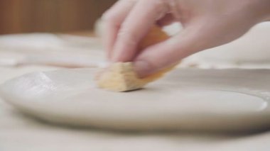 Potter Beyaz kil - yuvarlak tabak ve sünger kullanarak bir ürün yapar